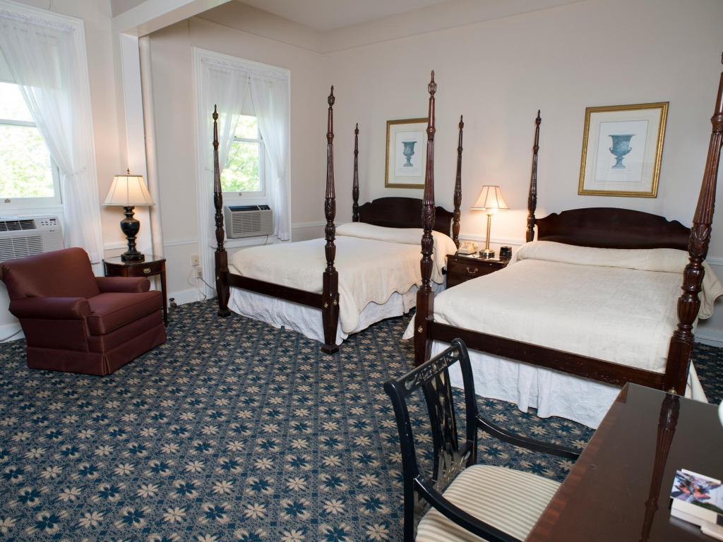A room with to beds with ornate wooden bed frames/ A patterned blue carpet and a red arm chair sit to the left.