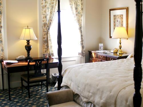 A detail shot of a room at the inn shows a small wooden desk with a chair and antique lamp next to a large window. A bed with wooden bed/